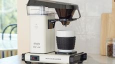 A silver Moccamaster cup one coffee maker, on a white counter. 
