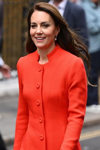 Catherine, Princess of Wales wears a red coat dress as she smiles during a visit to the Dog & Duck Pub to speak to members of staff to hear how it’s preparing for the Coronation Weekend during their visit to Soho on May 04, 2023 in London, England.