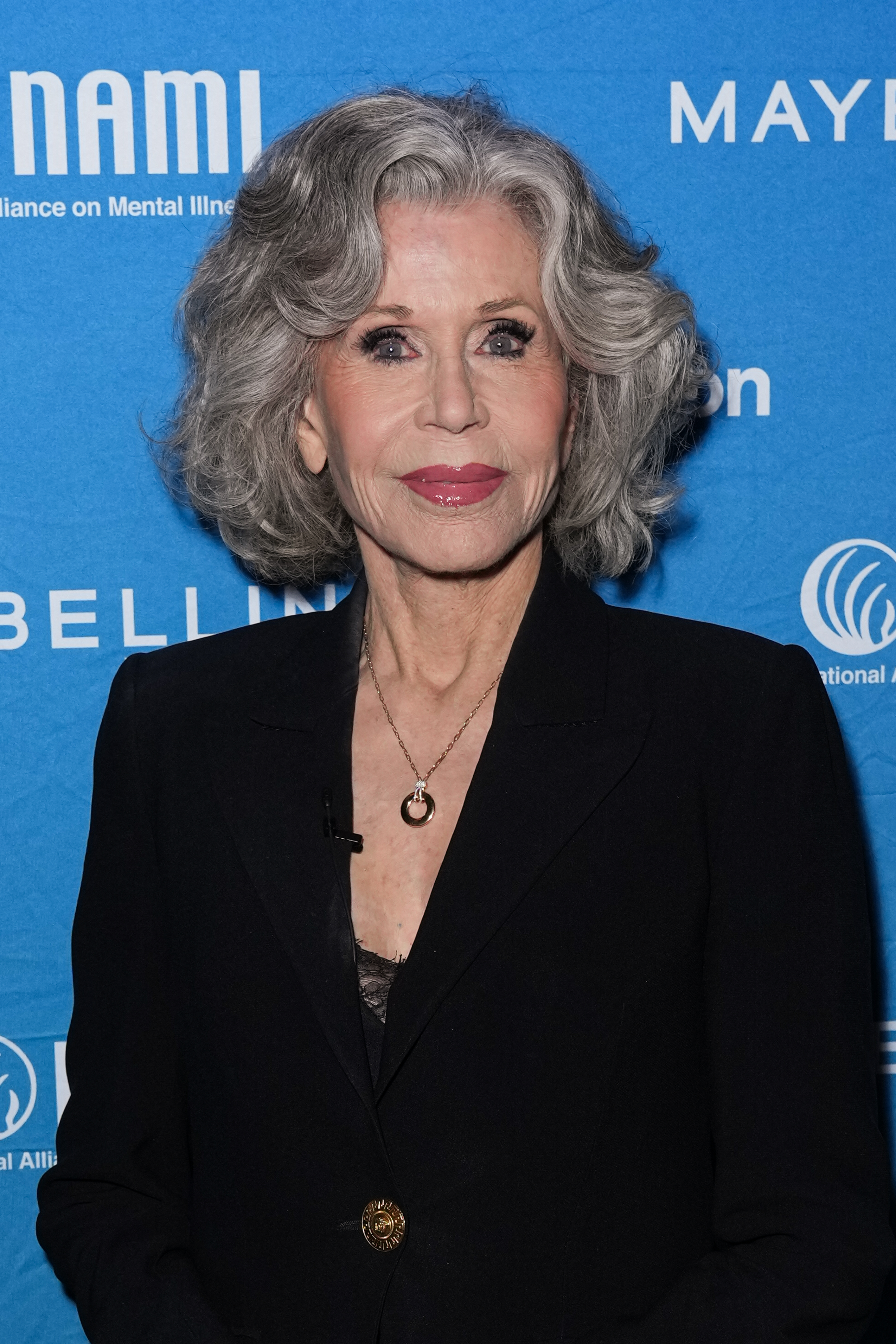 a white woman with gray hair wearing a black blazer and posing in front of a blue background