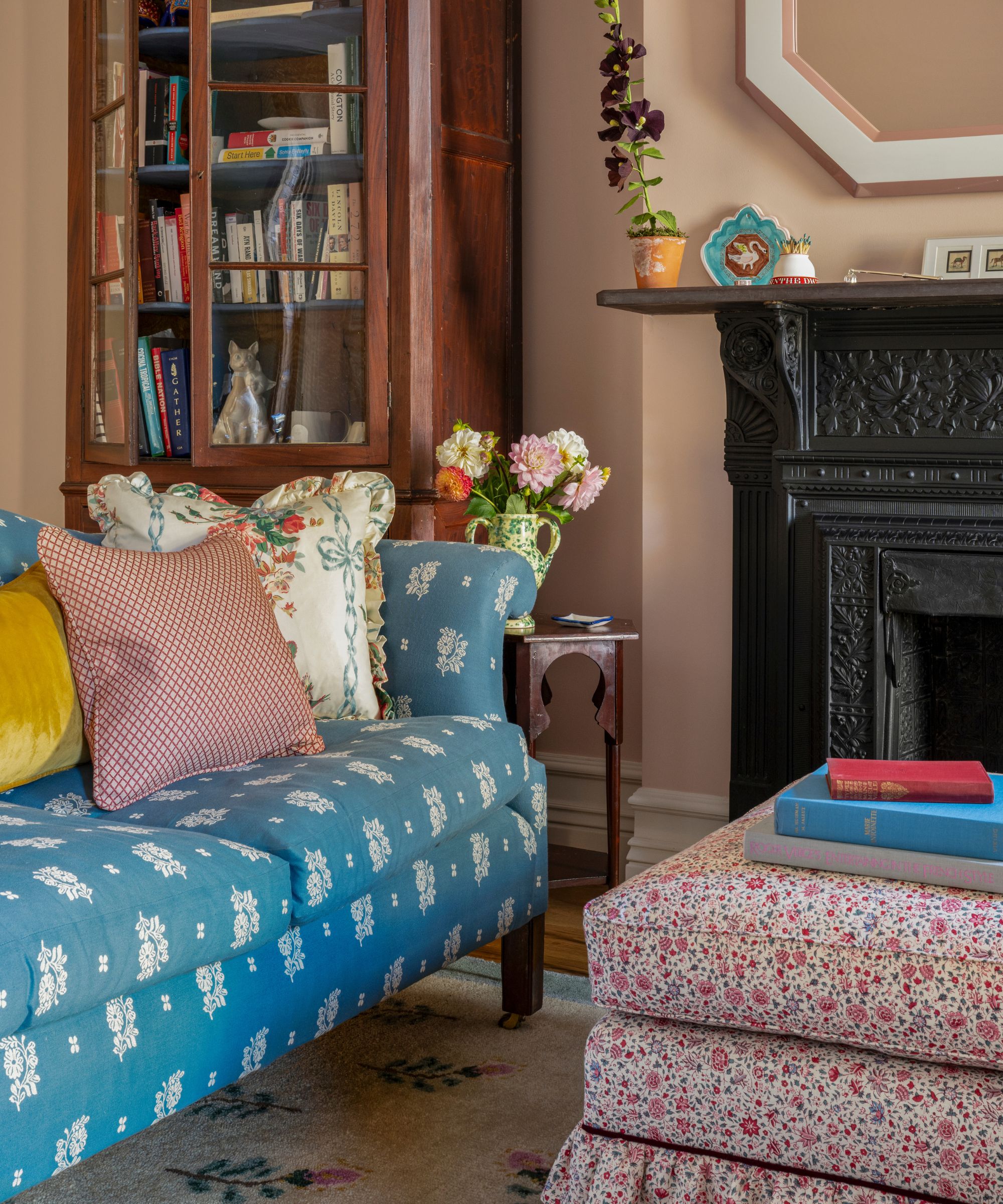 a pink home office with a black fireplace, antique dresser, vintage-style blue floral sofa and ottoman