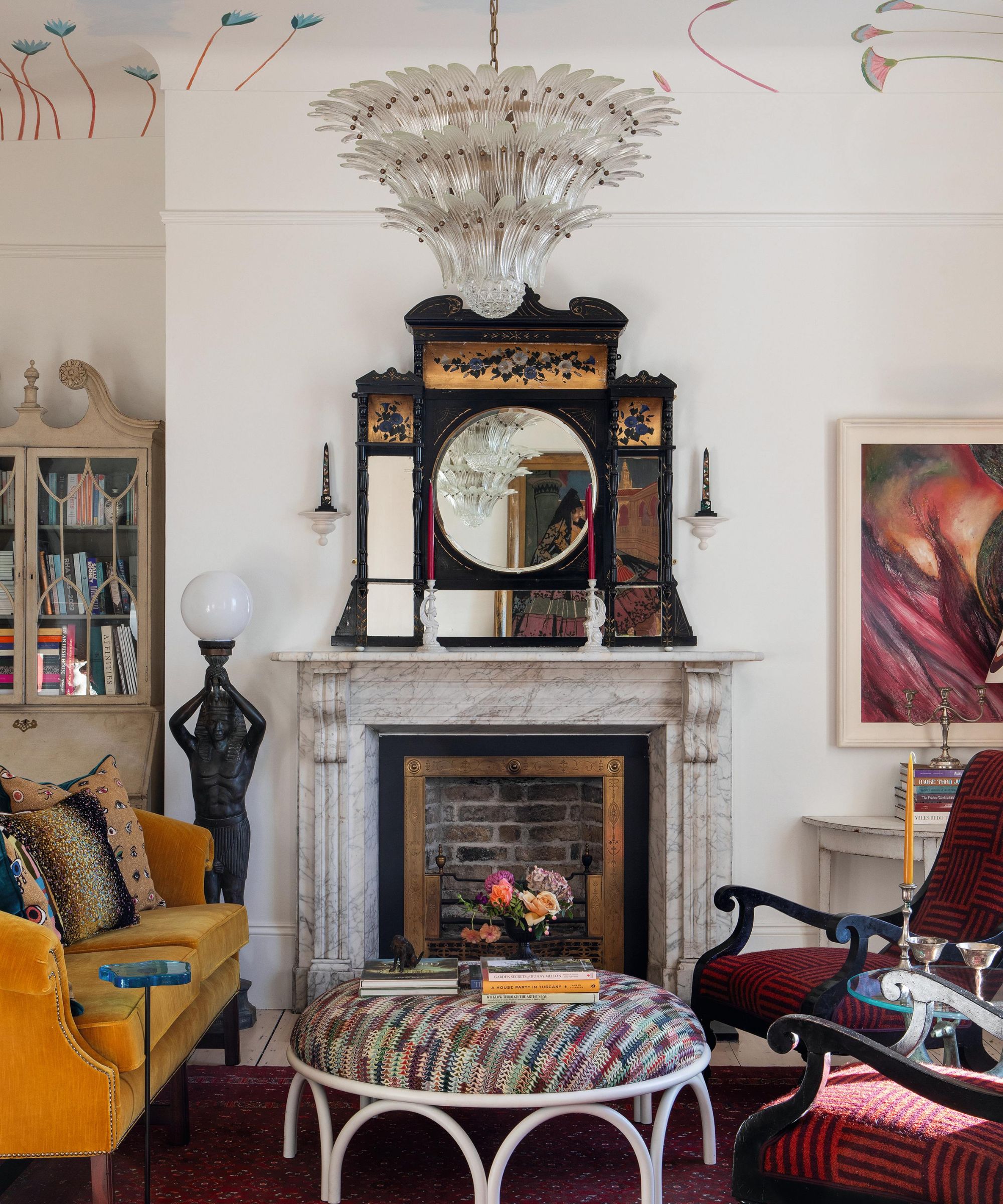 a grand drawing room with a painted ceiling, murano chandelier, marble fireplace, burgundy rug and chairs and an ochre coach