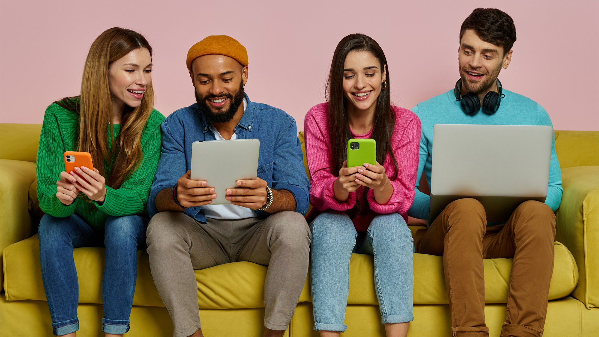 Studio shot of young people using technologies and smiling while sitting on the couch together