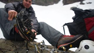 Man sitting on rock fitting crampons to hiking boots