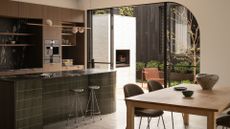 A kitchen and dining space with a green tiled island, chrome stools, a wood dining table, and a pendant light beside glass doors leading to an outdoor living room