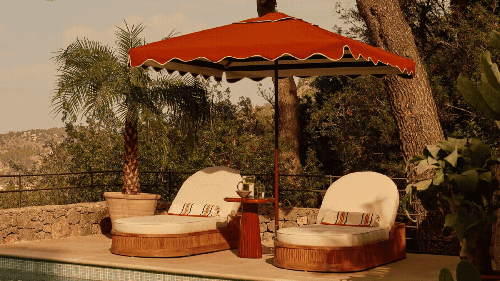 Soho Home outdoor collection by the pool, sofas, loungers, parasols, and side tables