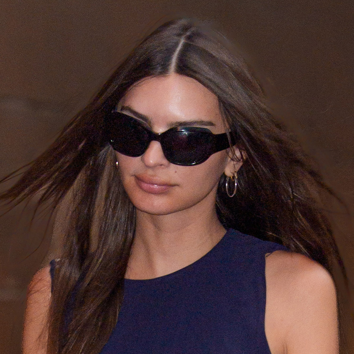 emrata wears sunglasses and a navy dress.