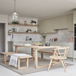 kitchen with wooden table and chairs sitting on a beige rug, with wooden open shelving and sage green cabinets