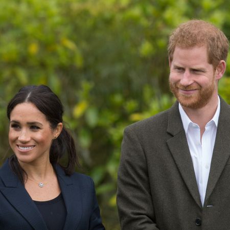 Meghan Markle wears a navy suit jacket with a black top and Prince Harry wears a white shirt with an overcoat