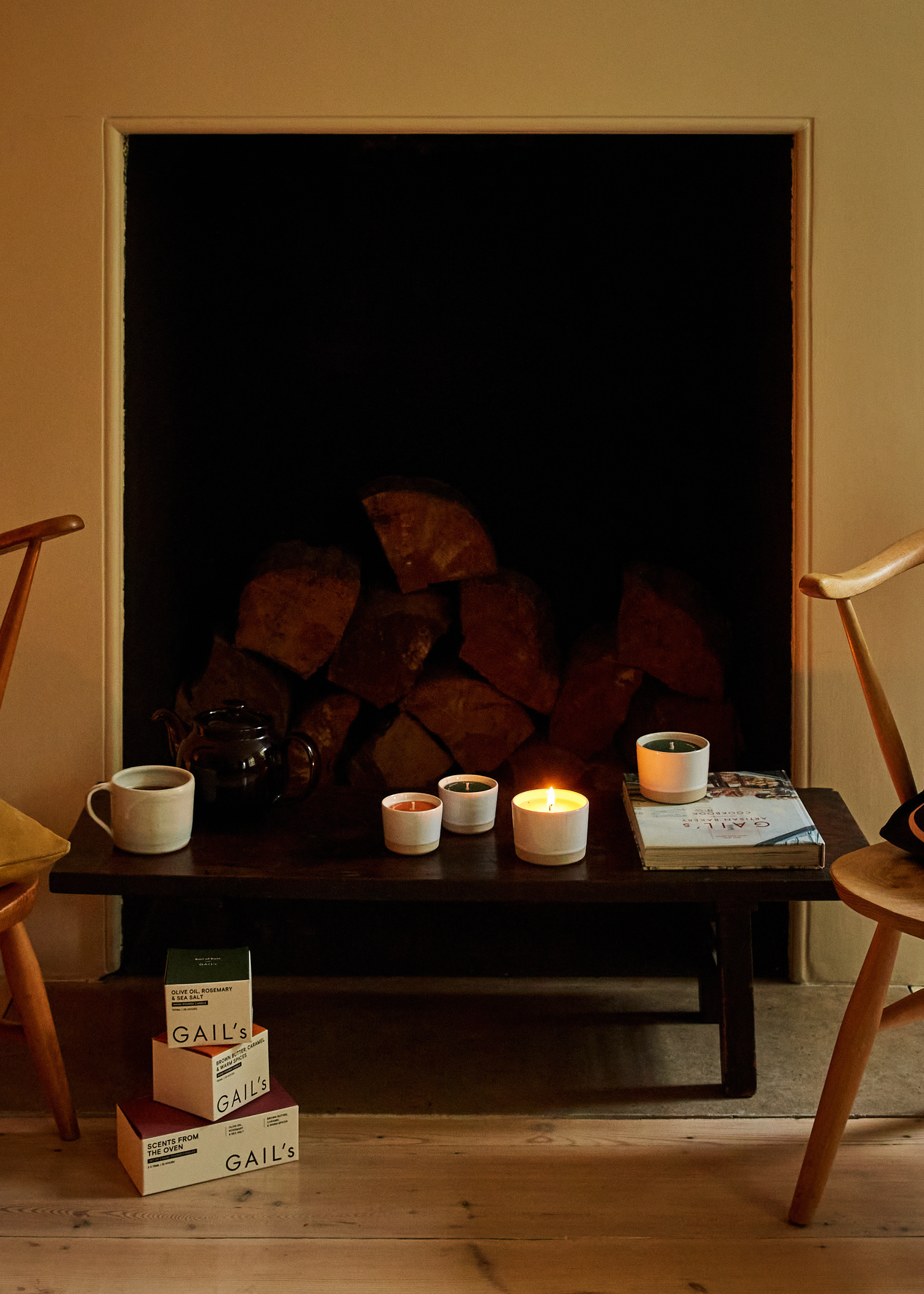 A fireplace with logs by a table with ceramic candles and a set of wood chairs
