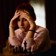 a young girl chess prodigy rests her head in her hands while playing chess in a still from the documentary queen of chess