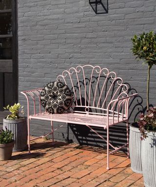 cobbled patio with pink metal garden bench against a gray painted wall