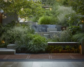 A sloping garden with stone levels leading upwards interspersed with evergreen planting