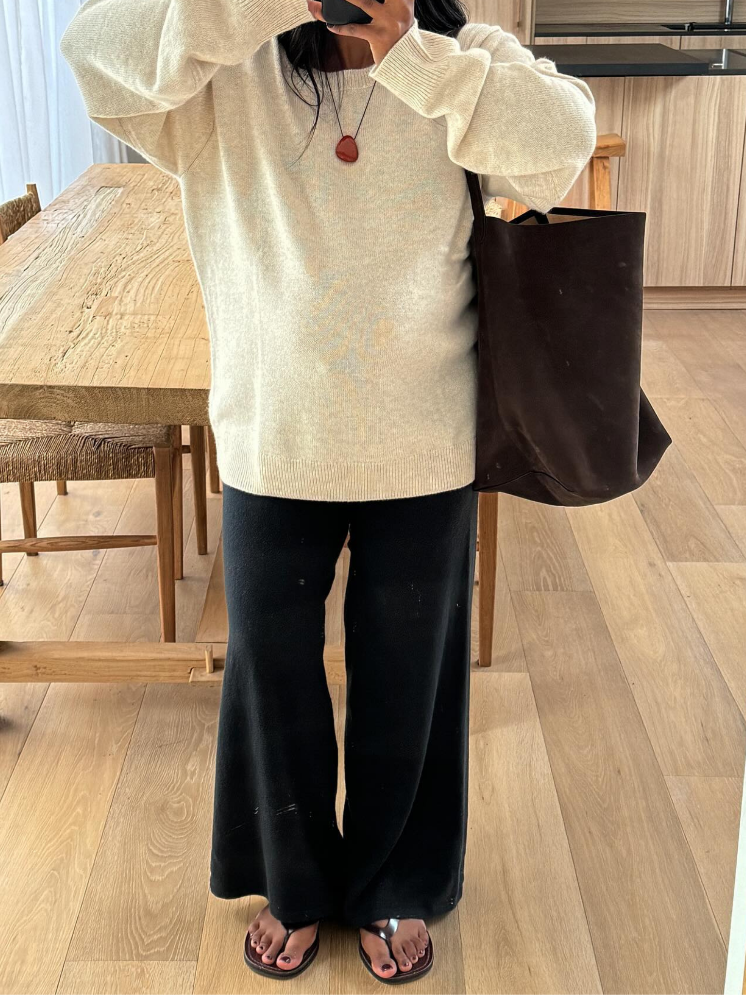 A woman taking a picture in a mirror, wearing flip-flops with a dark brown pedicure.