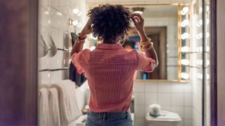 Woman looking in the mirror in the bathroom, touching her hair