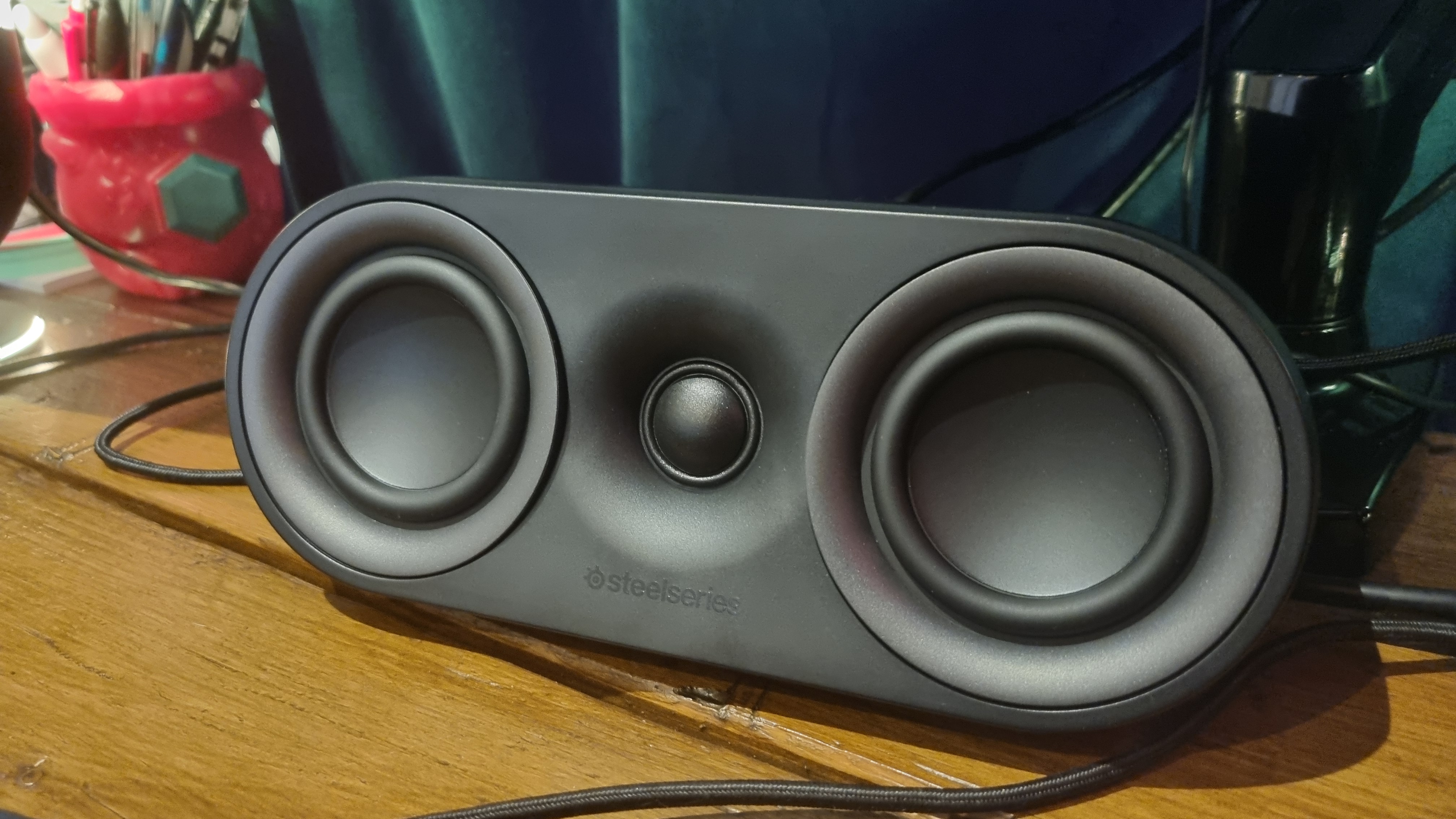 The central speaker of the SteelSeries Arena 9, on a wooden desk