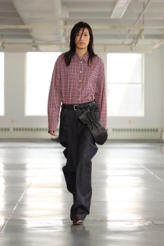 A Tibi Fall 2025 model wearing a flannel outfit, jeans, and belt.