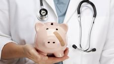 A female doctor holds a piggy bank that has a bandage on its cheek.