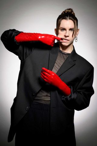 A portrait of Lynn Gunn with red gloves hooking her mouth with her finger