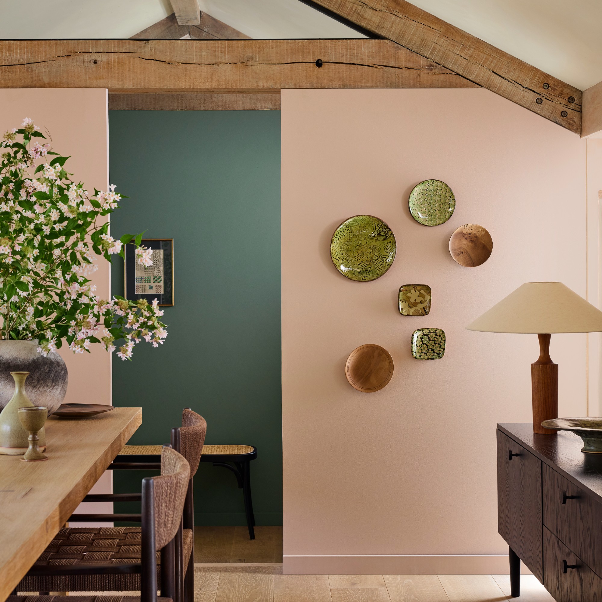 A dining room with beams and a midcentury-style sideboard with a partition wall painted in Little Greene Masquerade pink