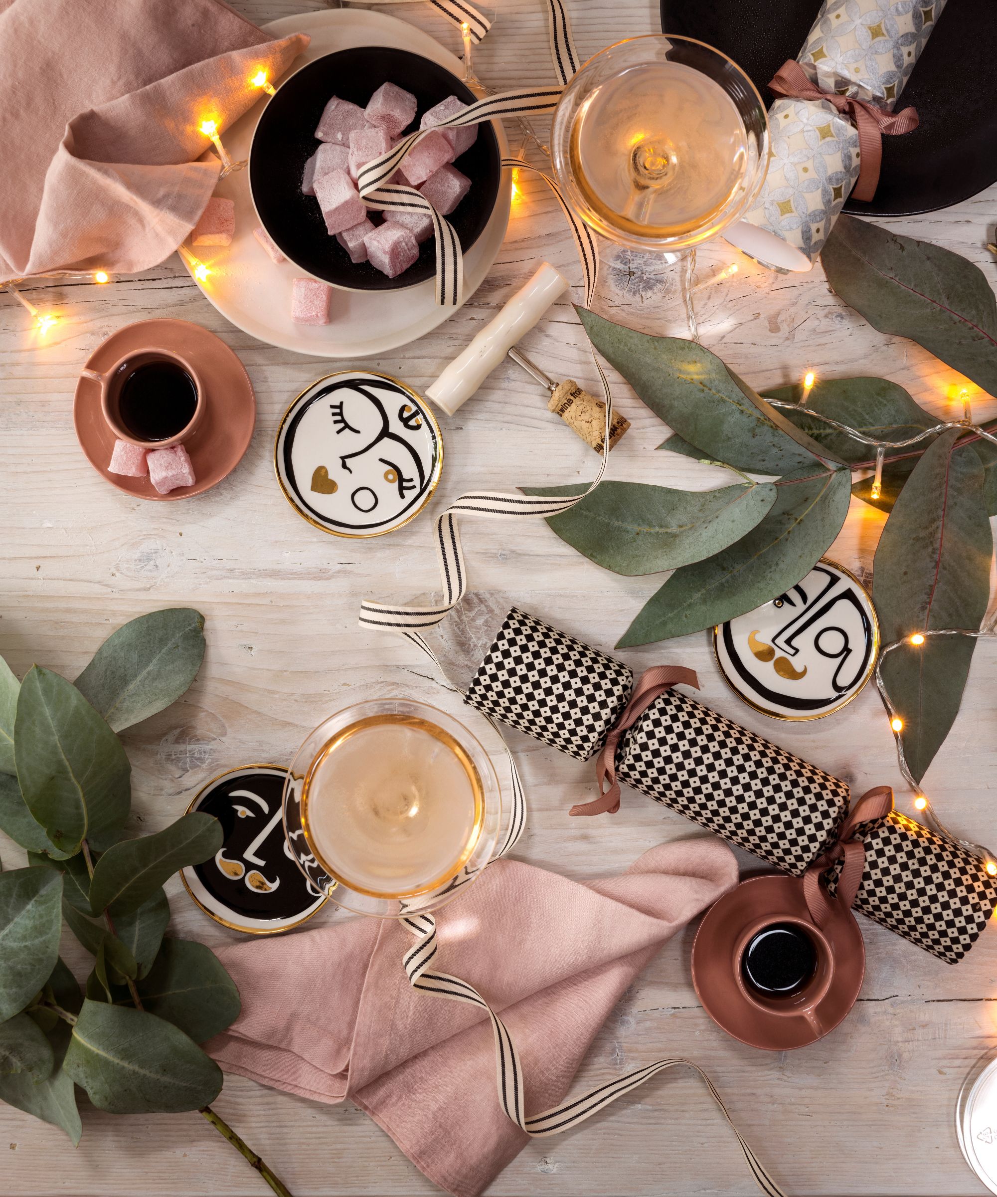 Black, white and pale pink table setting for Christmas with eucalyptus leaves and string lights