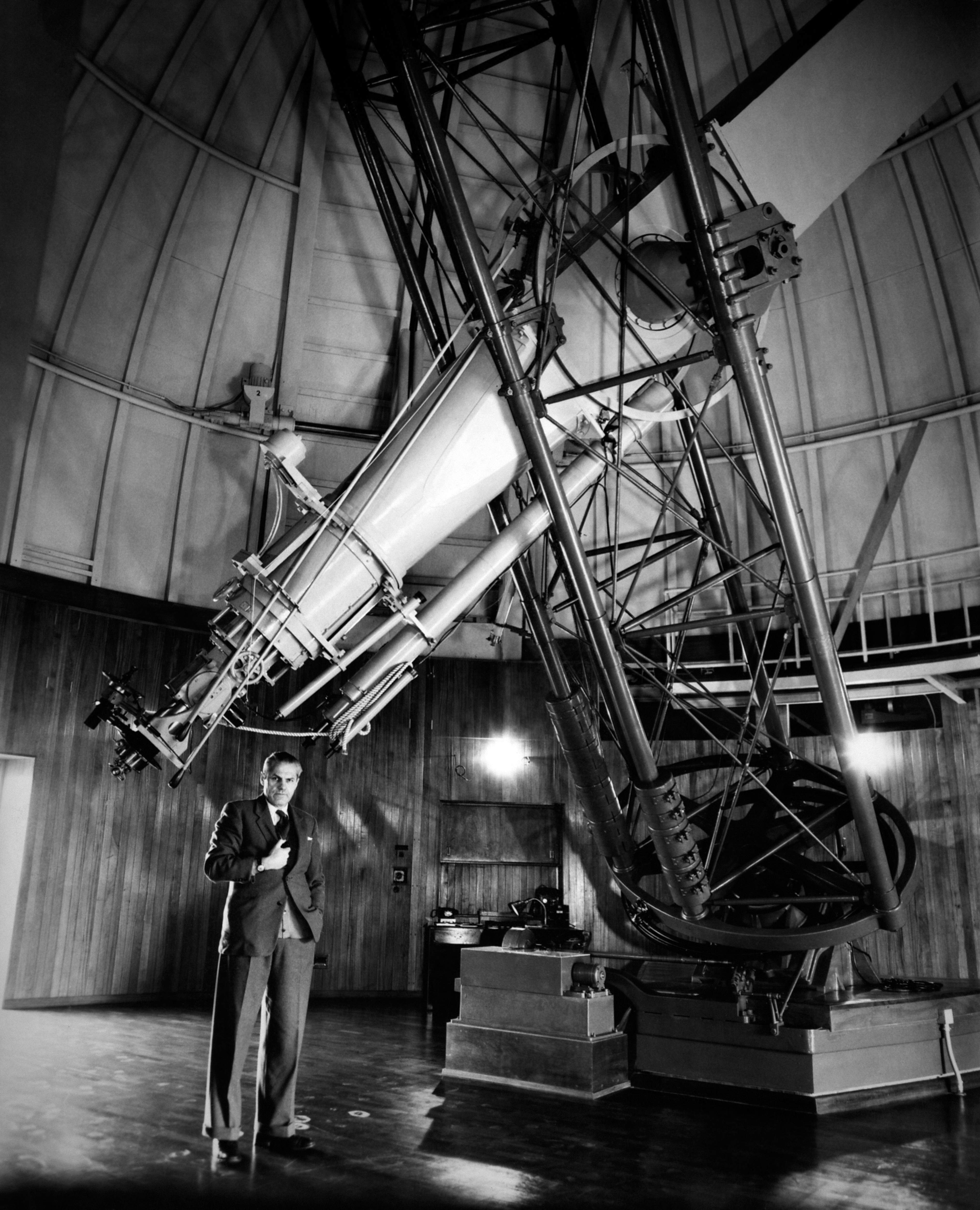 A large telescope score at the top right of the black and white photographs as a person standing underneath it.