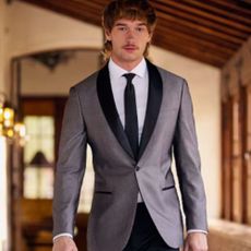 Young man in silver suit with black tie and lapel, walking down dimly lit barn-style corridor.