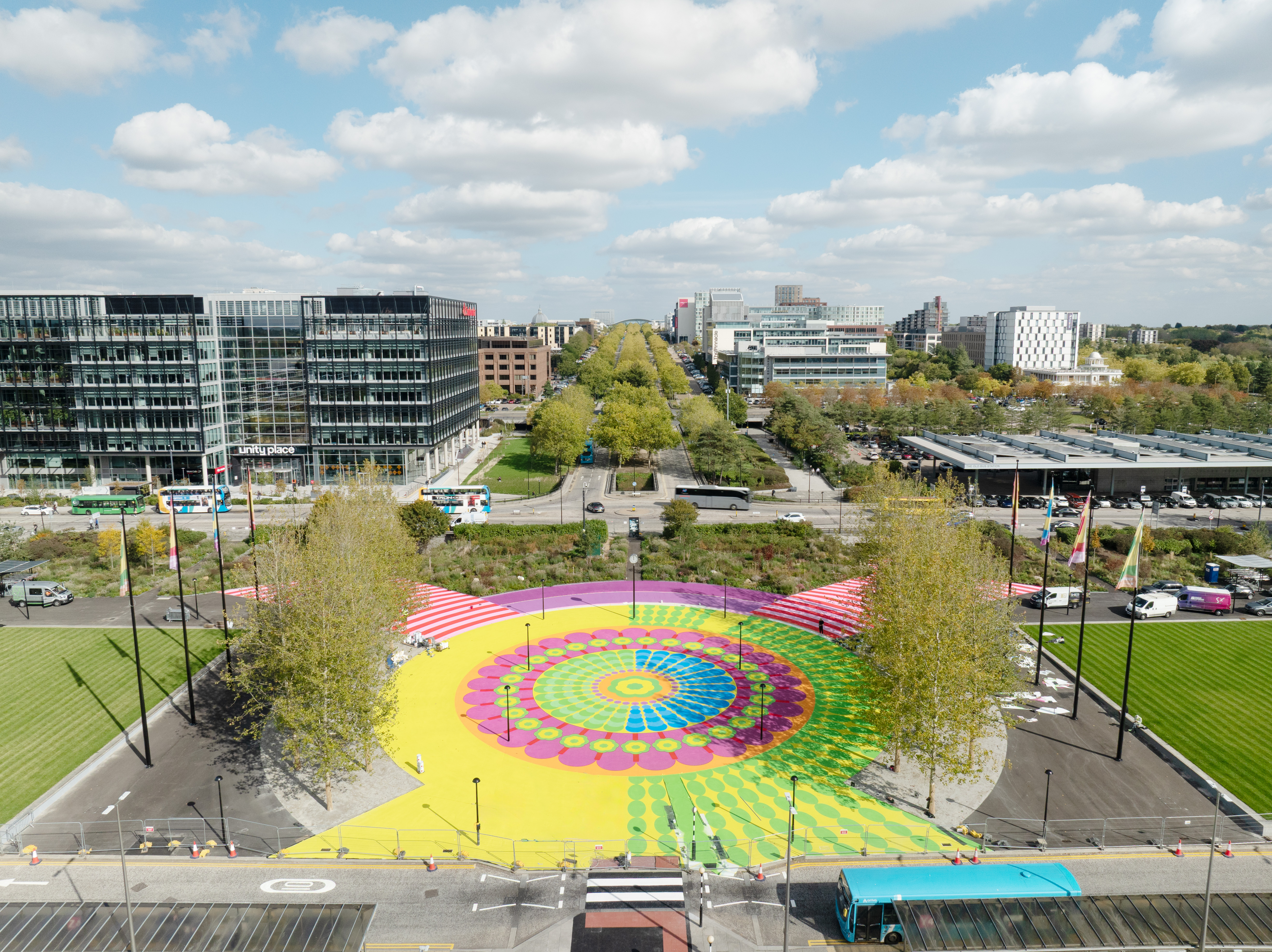 An aerial view of a concentric, colorful, and flower-like mural immersed in greenery.
