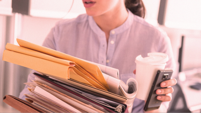 A woman carrying a stack of files and a coffee