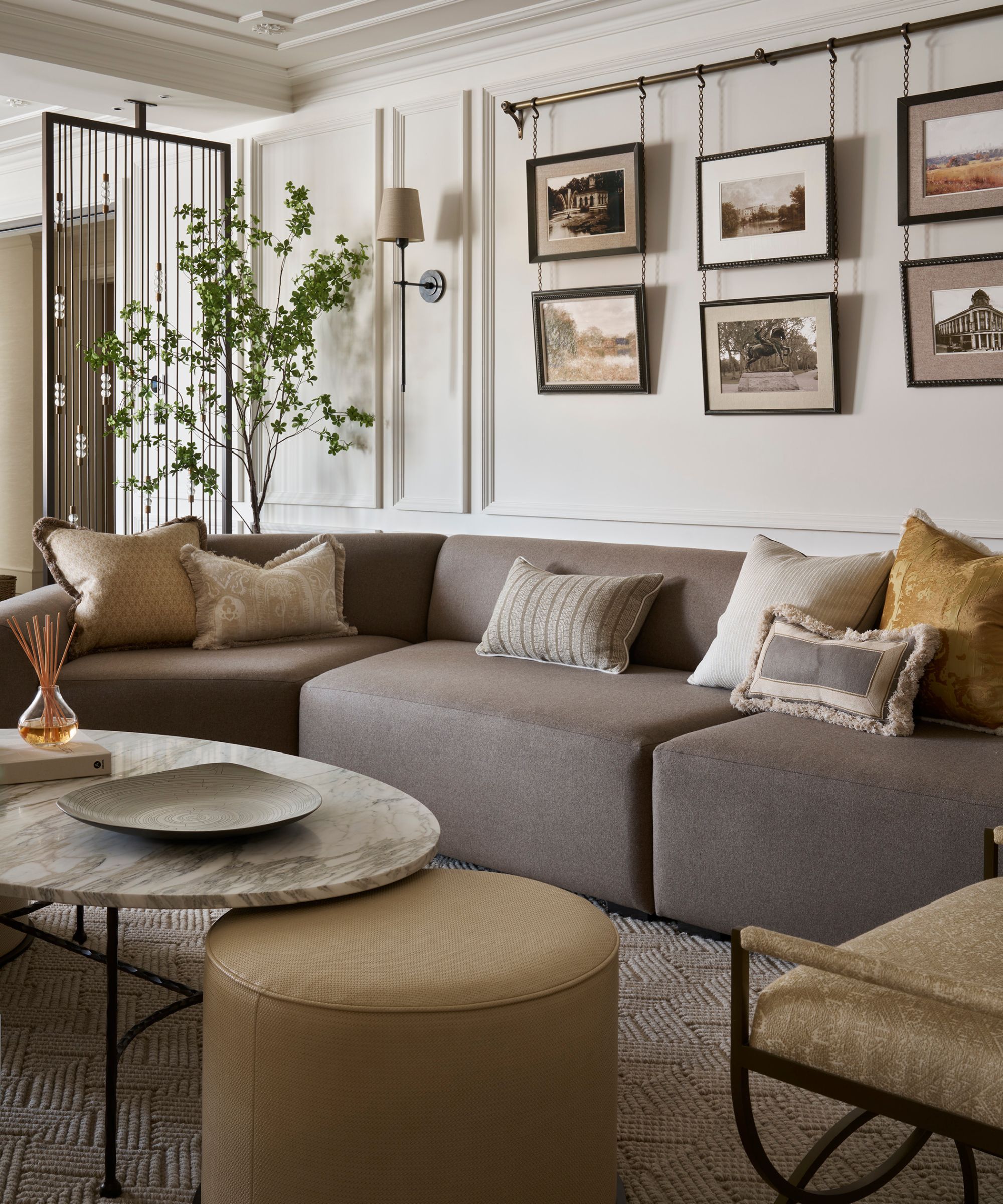 a quiet luxury neutral living room with a low slung grey modular couch, a marble coffee table, pouffe, and wall moldings with a traditional wall art hanging pole