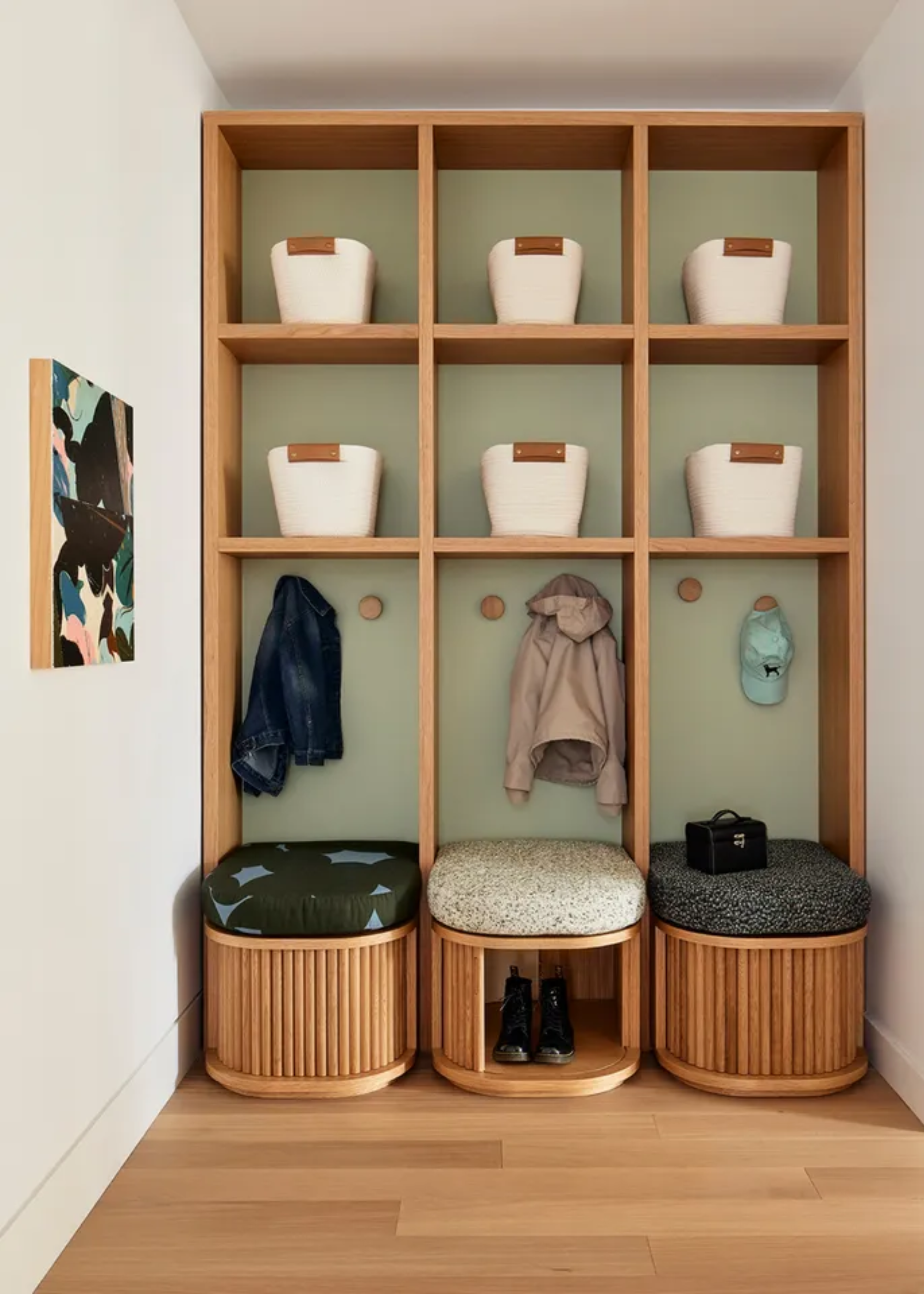 An entryway with wooden shelving, storage bags, hooks for hanging coats, three seats, and tambour doored shoe storage