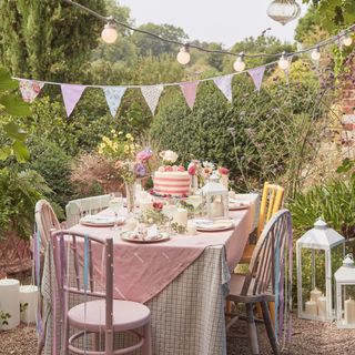 garden party with festoon and pendant lighting, bunting, pastel colours, large cake, flowers, lanterns, candles