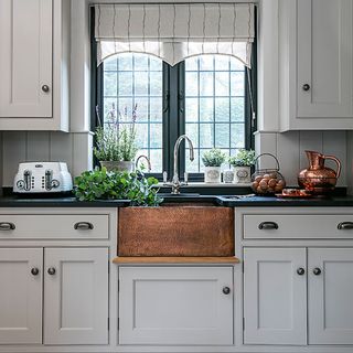 grey kitchen with copper sink, window with roman blind and a stainless steel tap