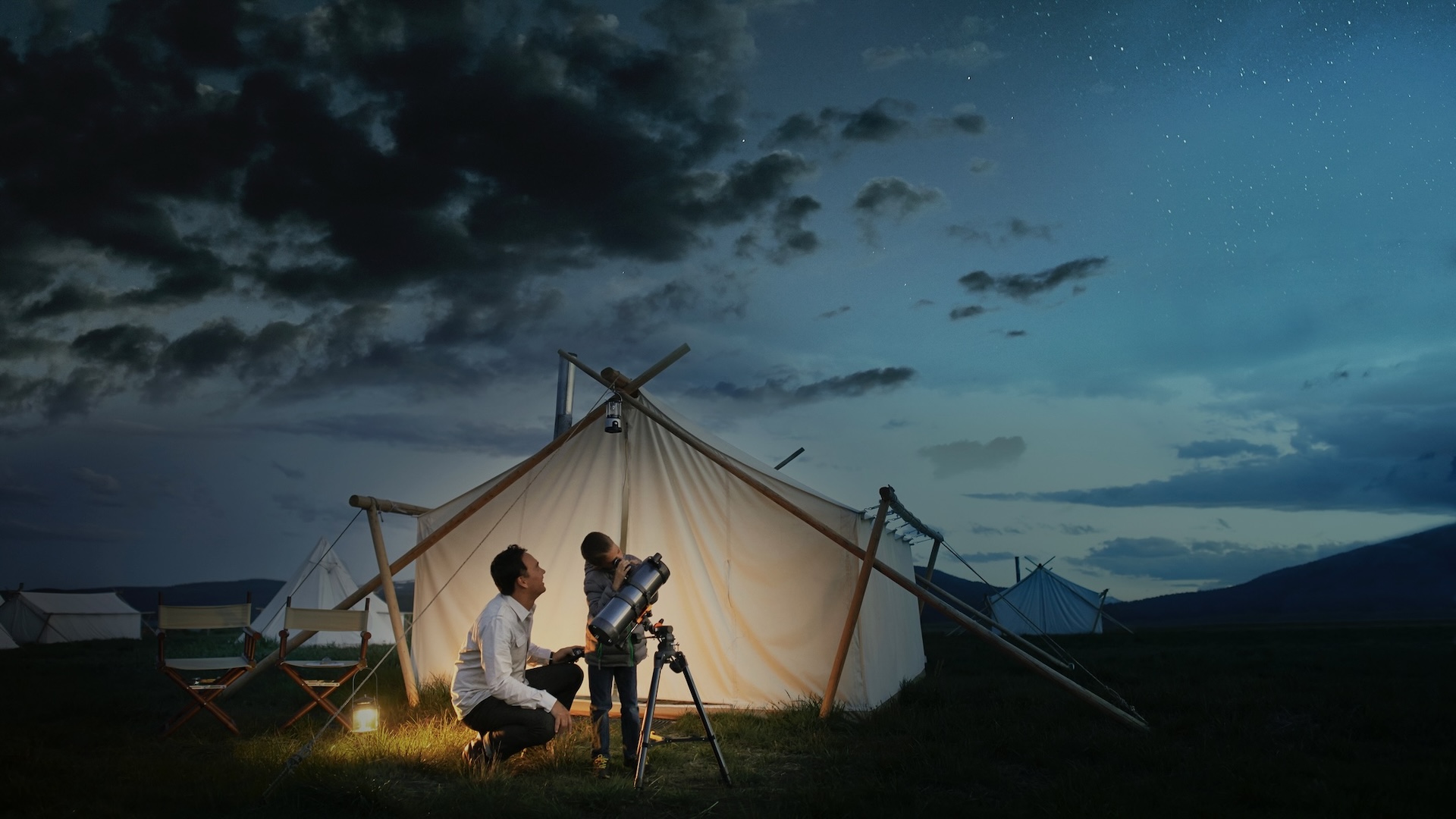 A parent and child using a telescope outside a tent