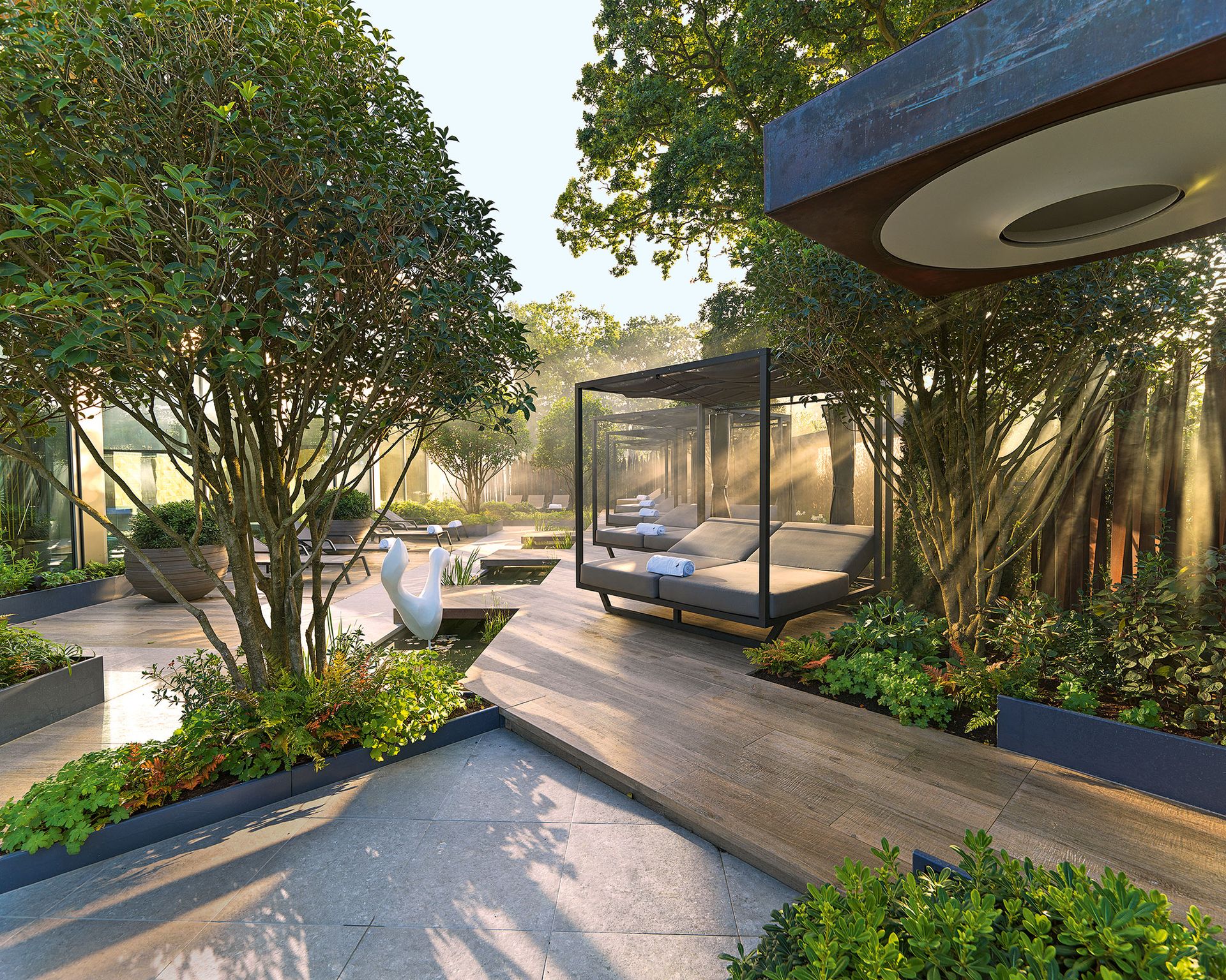 Modern, futuristic garden with stone paving, wooden decking, glass buildings, trees and planters