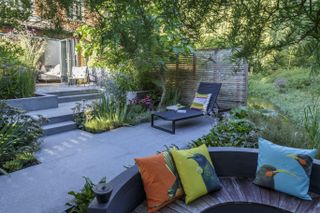 Sunken patio furniture ideas in a shaded, gray-paved garden with overhanging trees.