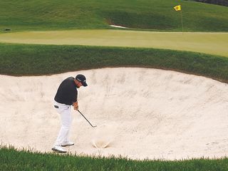 Shane Lowry at impact hitting a golf ball out of a greenside bunker towards the flag