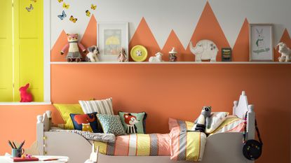 A children&#039;s bedroom with an orange mountain-like painted mural and striped bedding on the bed