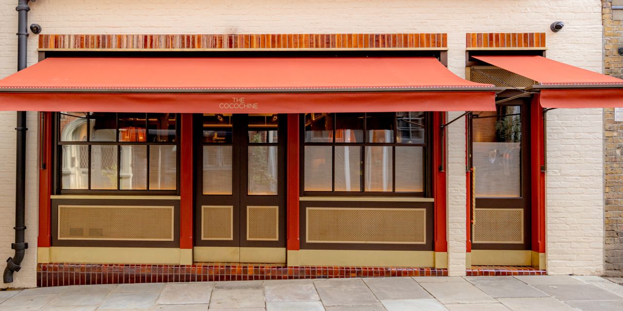 The red, wood, and gold exterior of a restaurant has a red curtain that reads &quot;The Cocochine&quot; in yellow.