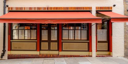 The red, wood, and gold exterior of a restaurant has a red curtain that reads "The Cocochine" in yellow.