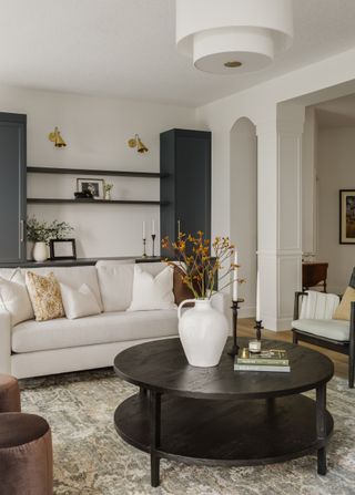 A living room with a round black coffee table, a cream couch, and a built-in blue-gray cabinetry and shelving