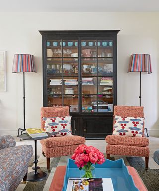 living room with black glazed cabinet, orange chairs with patterned cushions and lamps with striped shades