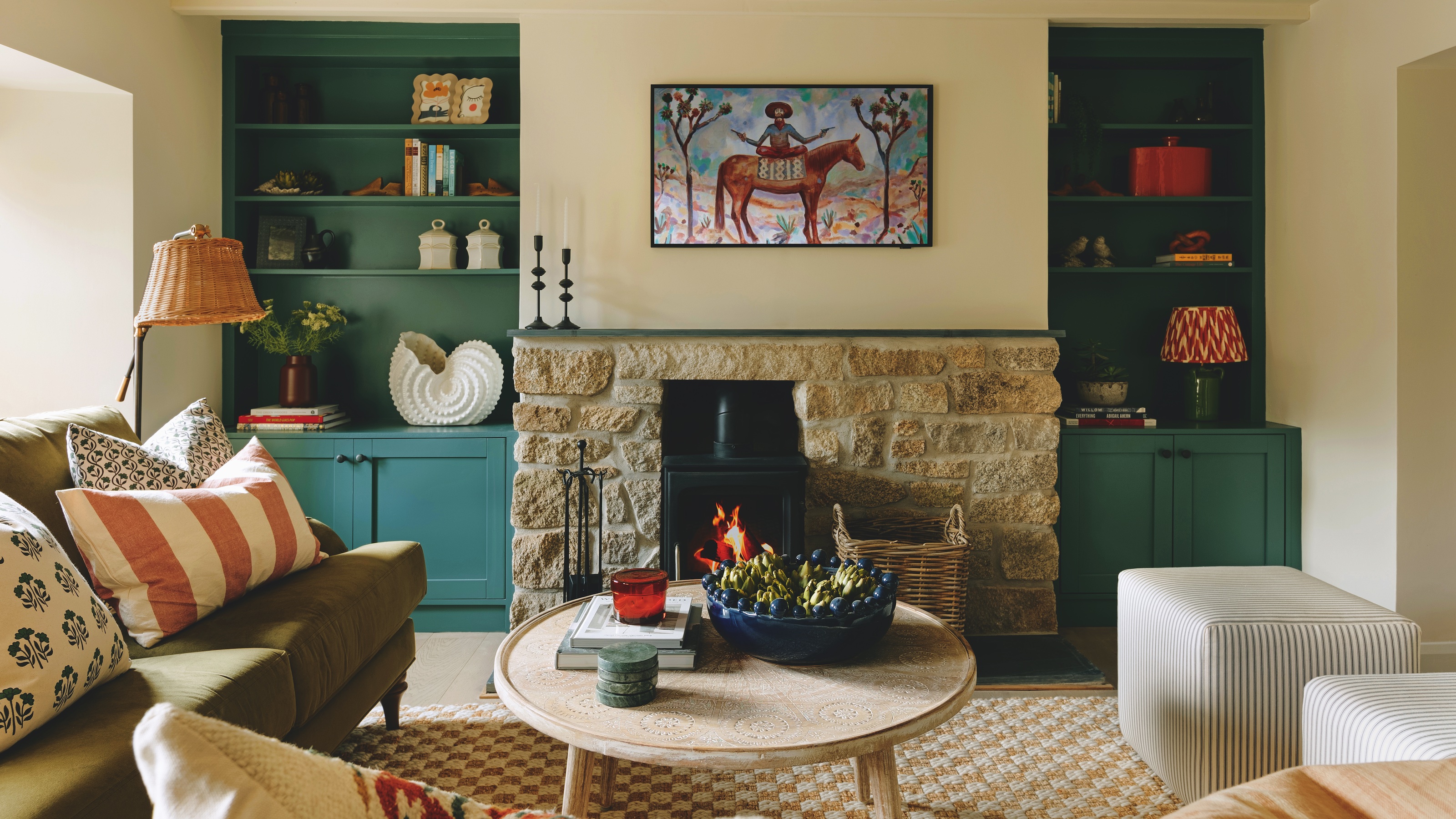 sitting room in cottage with stone fireplace and built-in cupboards in alcoves painted teal