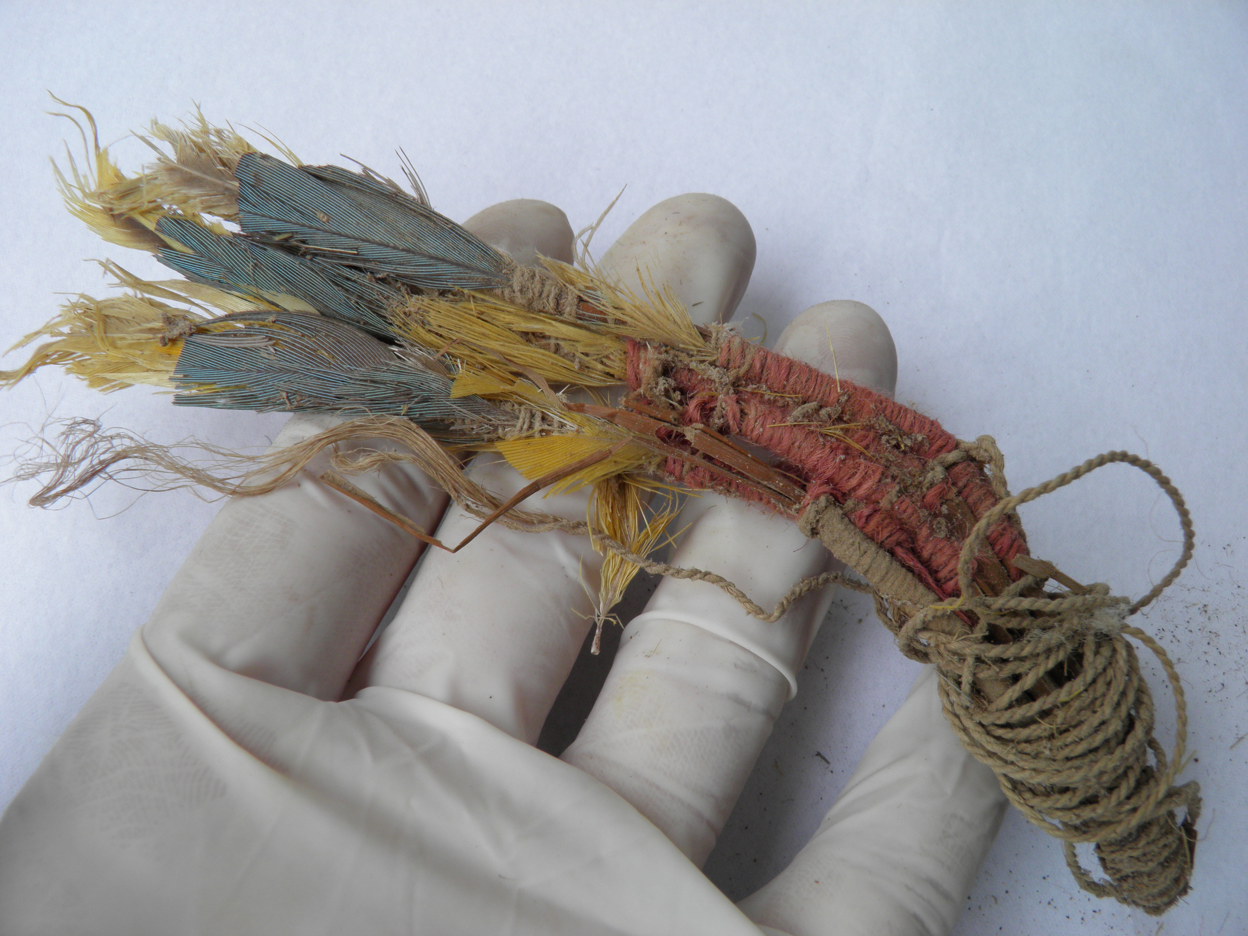 A bundle of red, yellow and blue feathers tied together with ancient rope and held by a gloved hand