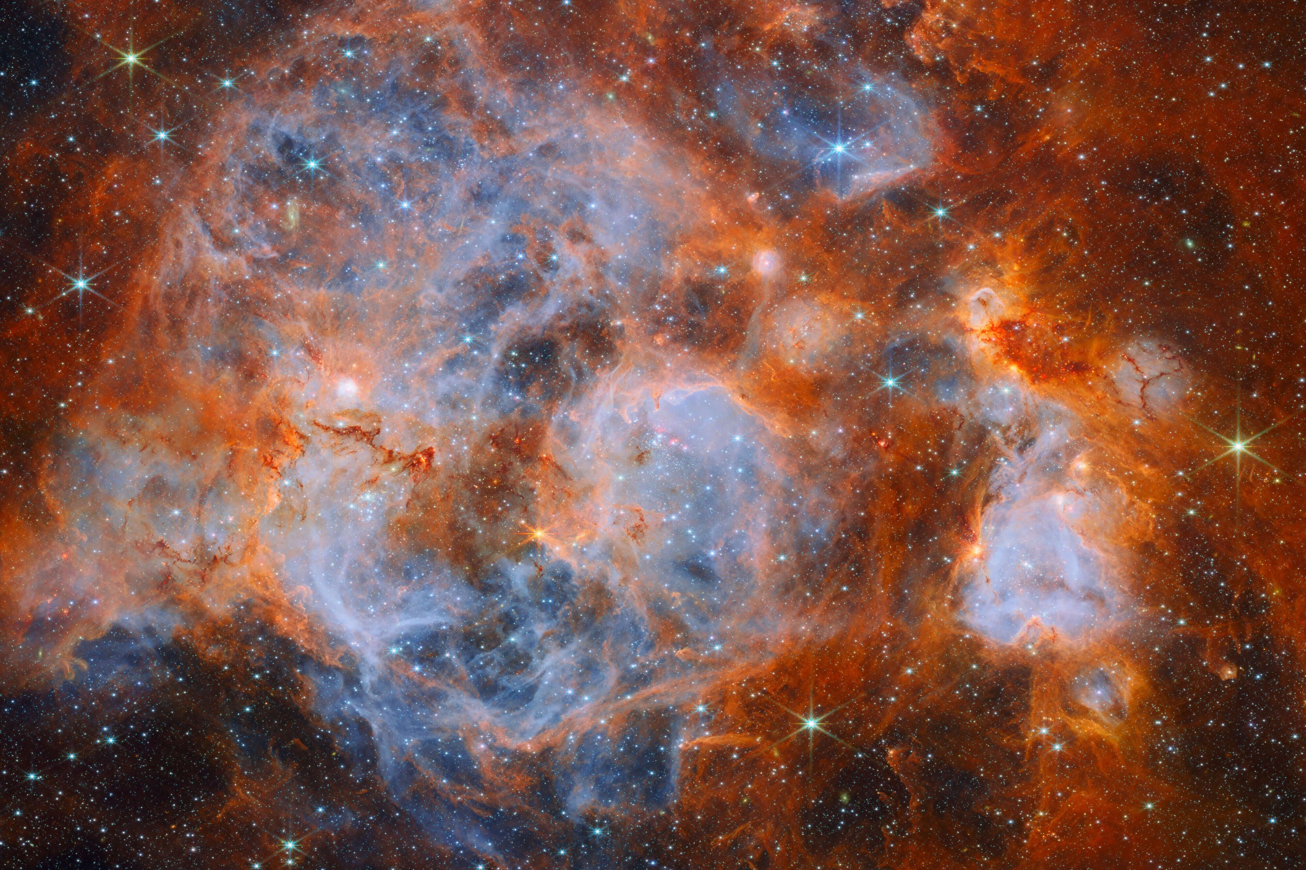 A nebula made of clouds of gas and dust with stars forming within. In the centre and out to the left it is filled with thin, wispy blue gas that forms delicate layers.