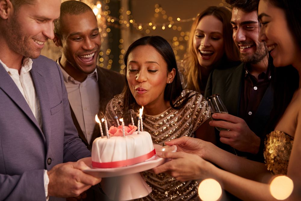 Attractive young people at a birthday party blowing out candles on a cake.