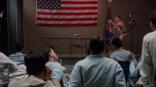 A group of people watch people playing ping pong in front of an American flag in Forrest Gump