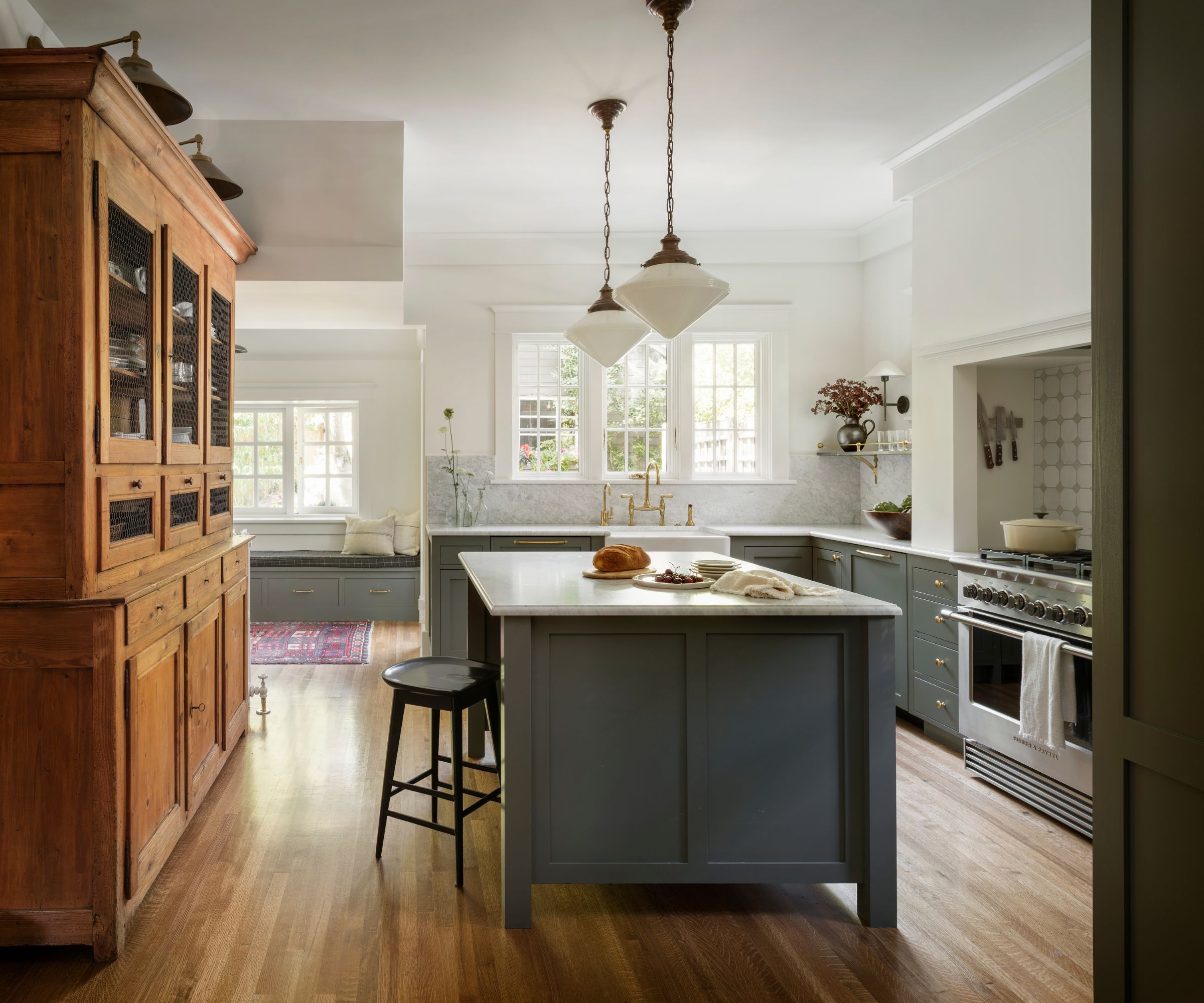 A craftsman kitchen with white walls, mid-green lower cabinets and island, and a large wooden dresser