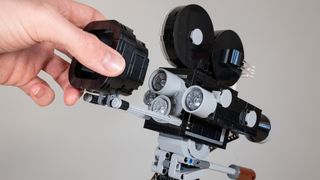 The Lego Disney Walt Disney Tribute Camera, a close-up of the 1920s film camera main build. A hand slides the matte box away to reveal the trio of lenses