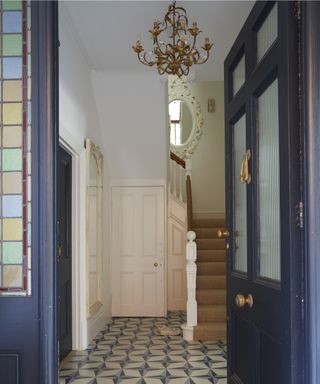Blue front door opening onto a Victorian hallway floor with a chandelier