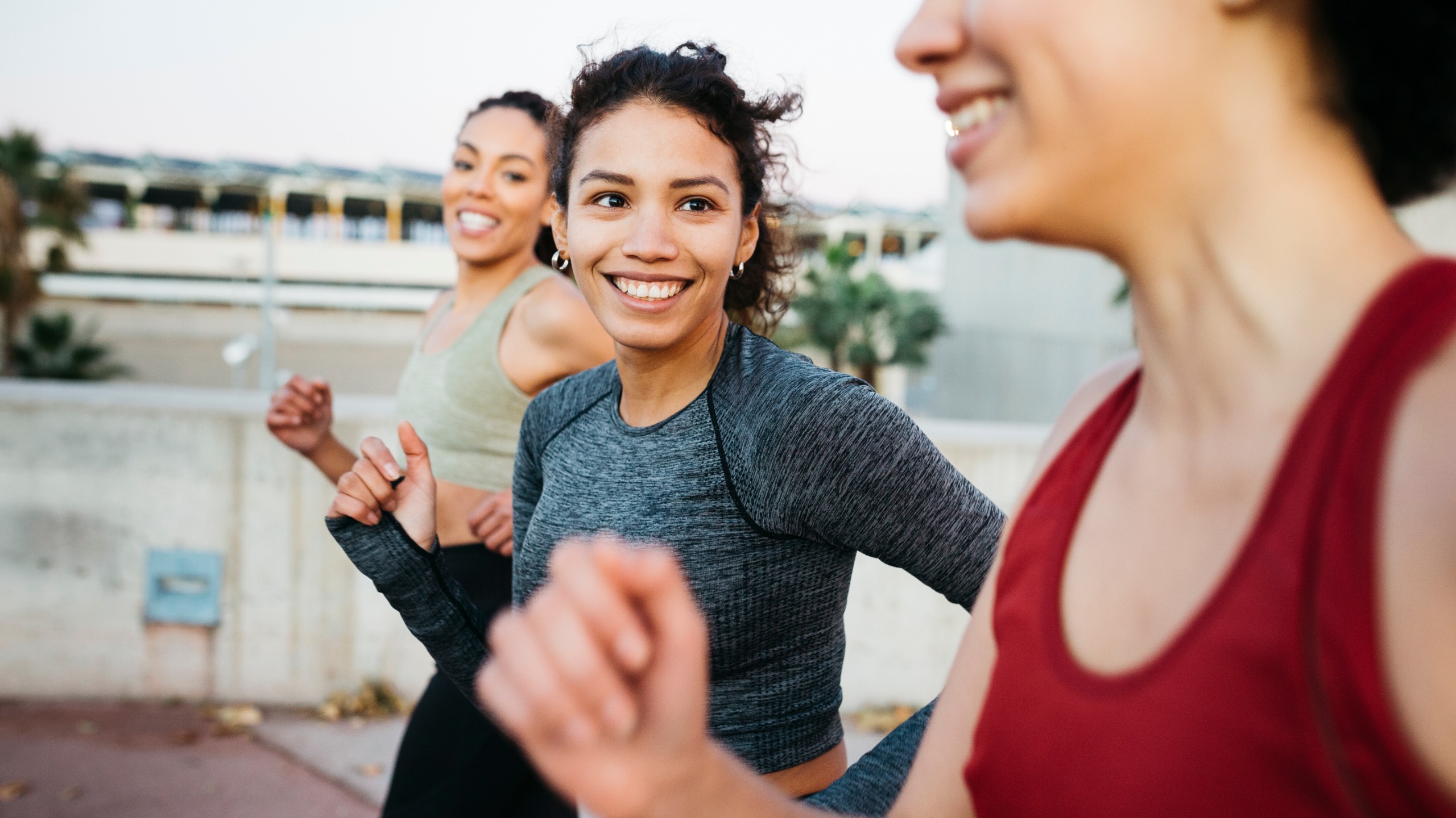 Three women smile as they run together. 